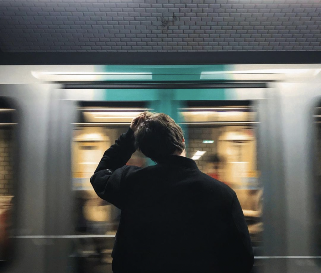 Un homme de dos se grattant la tête en regardant passer le métro parisien