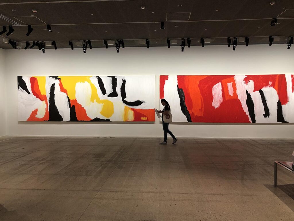 jeune femme visitant l'exposition Sally Gabori à la Fondation Cartier. Derrière de toiles immenses et colorées