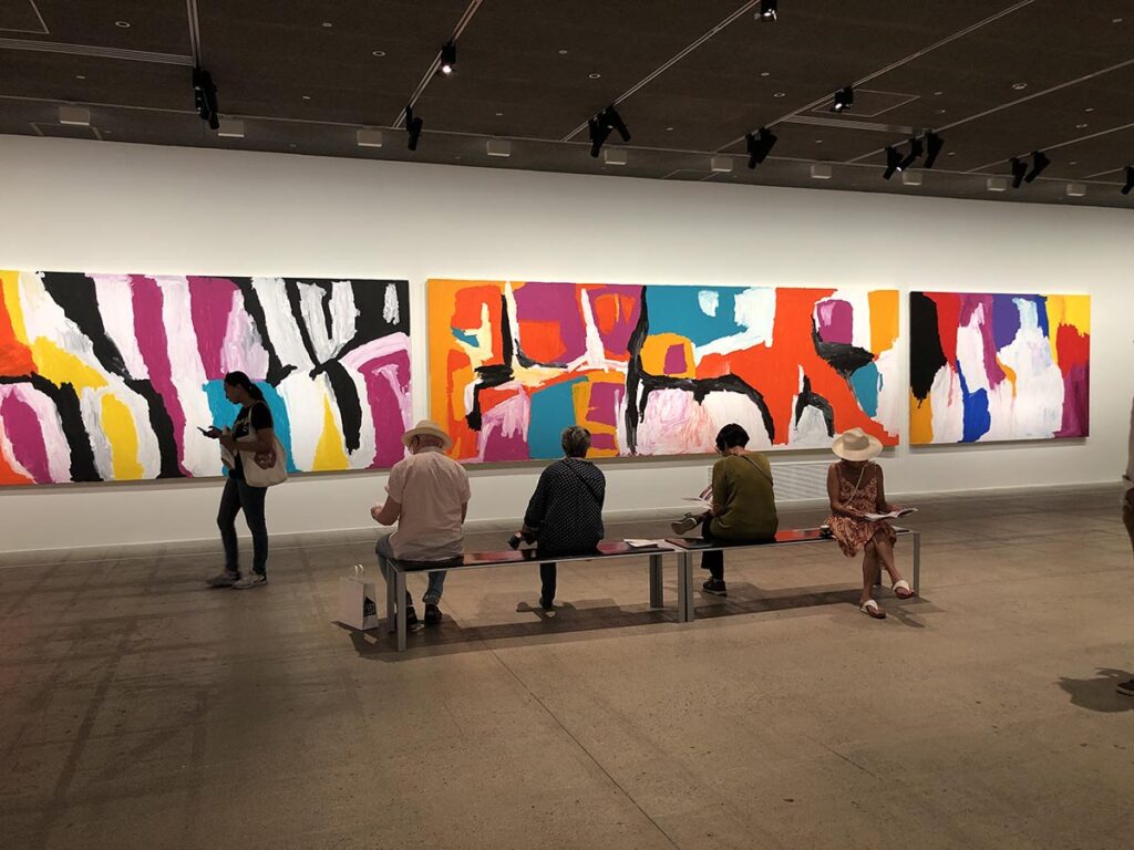Plusieurs personnes assises sur un banc devant les immenses toiles de Sally Gabori à la Fondation Cartier