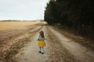 une petite fille marche sur un chemin de campagne. Elle porte une robe chasuble jaune sur une chemisette bleue. Comme un retour aux sources