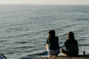 deux femmes regardent la mer accroupies sur la plage - elles symbolisent l'amitié