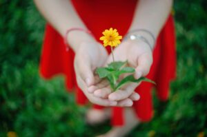 une jeune femme en robe rouge tient une fleur jaune dans les mains symbole de joie